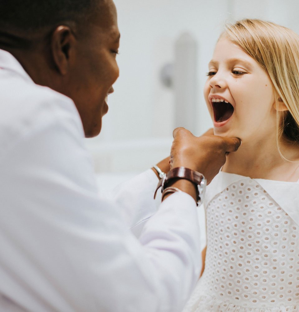 Doctor examining a young girl's throat with a tongue depressor.