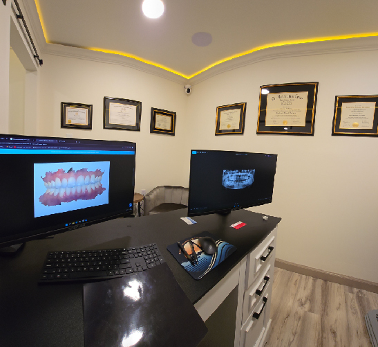 Dental office with computer screens displaying dental images and certificates on the wall.