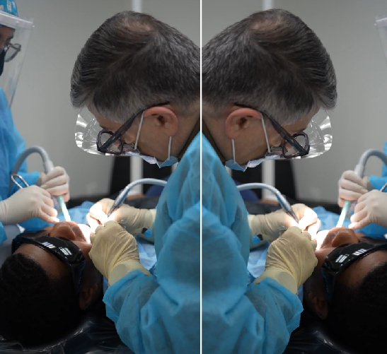 Dentist treating a patient wearing blue protective gear and mask.