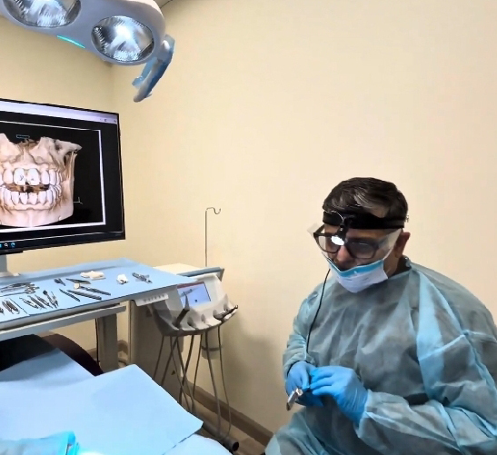 Dentist wearing protective gear working in a dental clinic with X-ray images.
