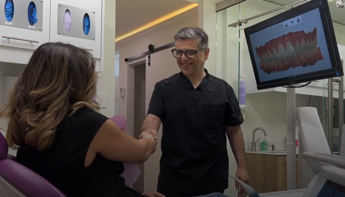 A dentist warmly shakes hands with a patient in a modern clinic.